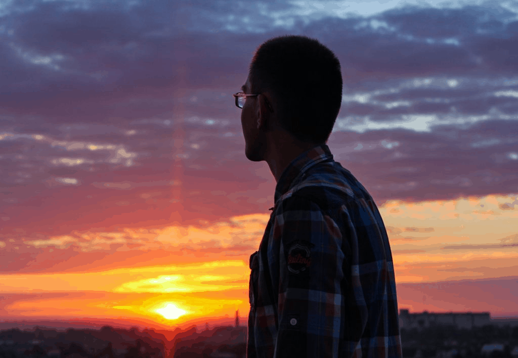 Young man with glasses looking at the sunset with motivation and determination
