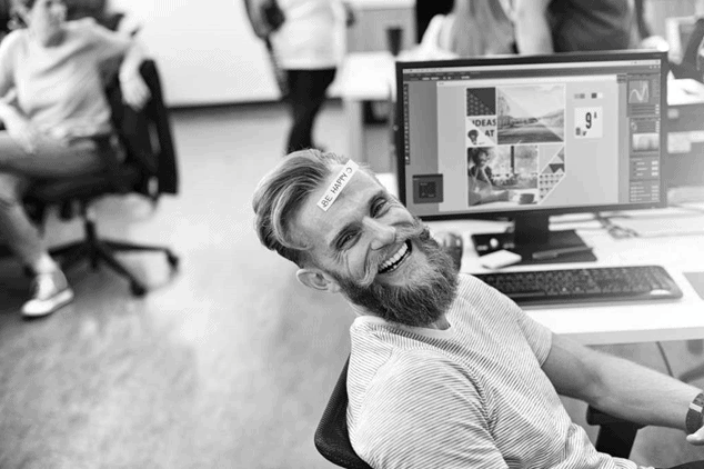 A cool young bearded guy having a lot of fun while he is working on his computer 