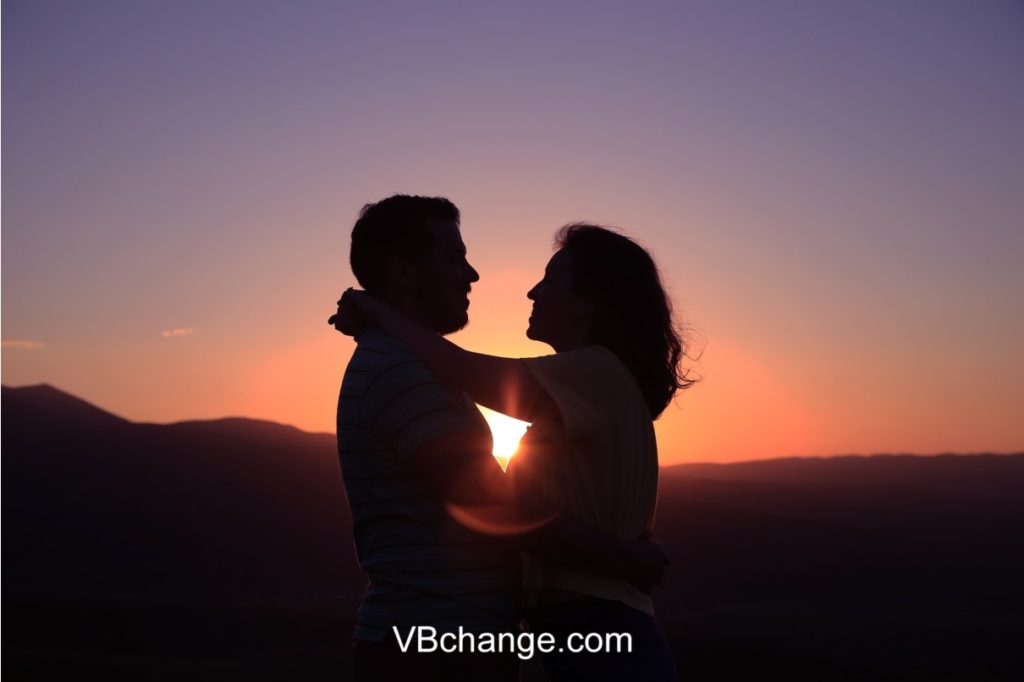 A loving couple holding each other in front of a beautiful sunset sharing love.
