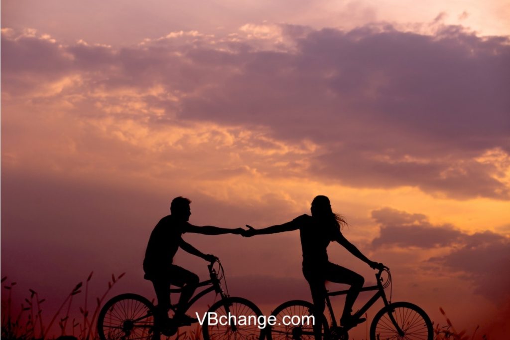 Romantic couple holding hands together while riding bicycle in the sunset
